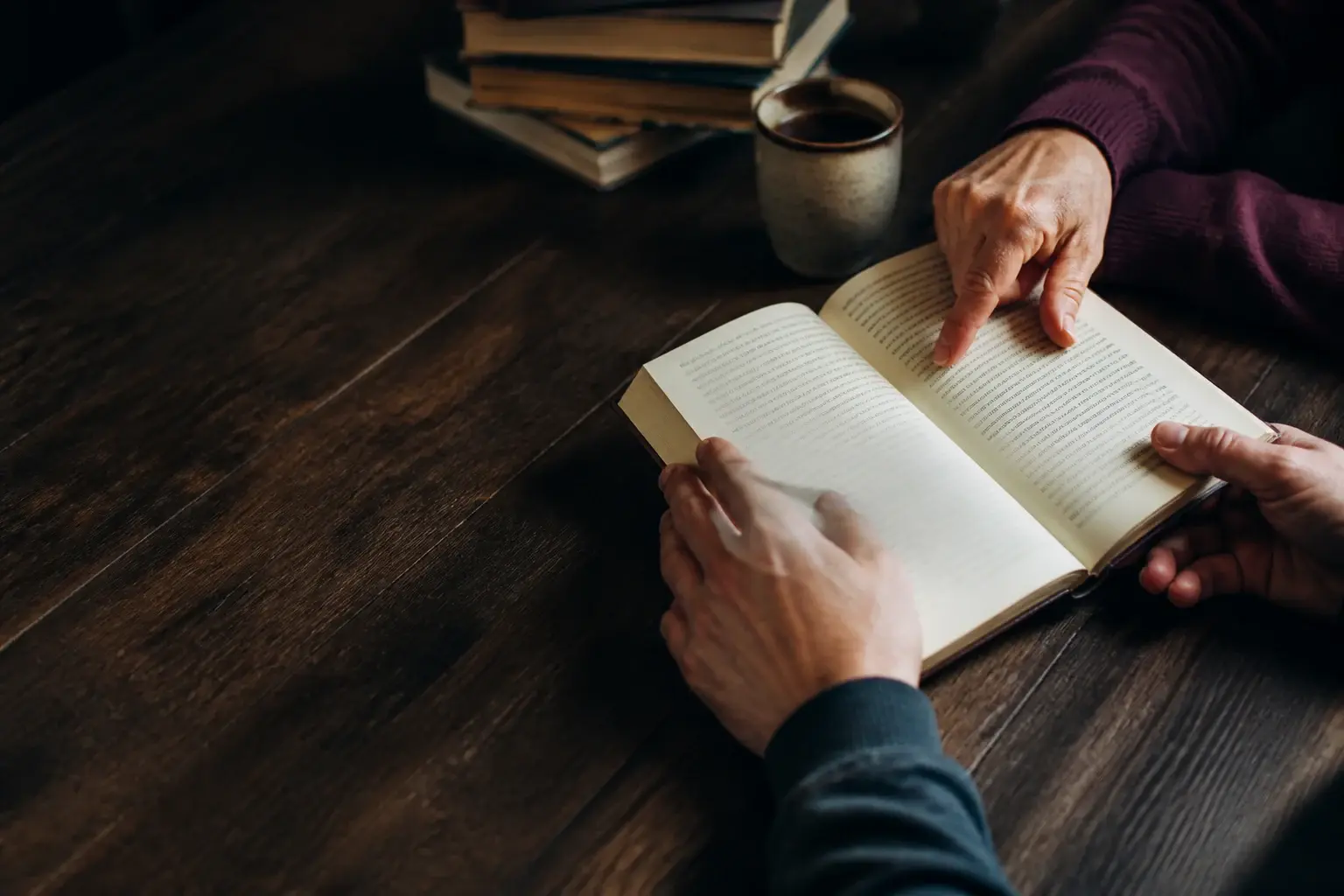 Readers sharing a book and conversation at a wooden table