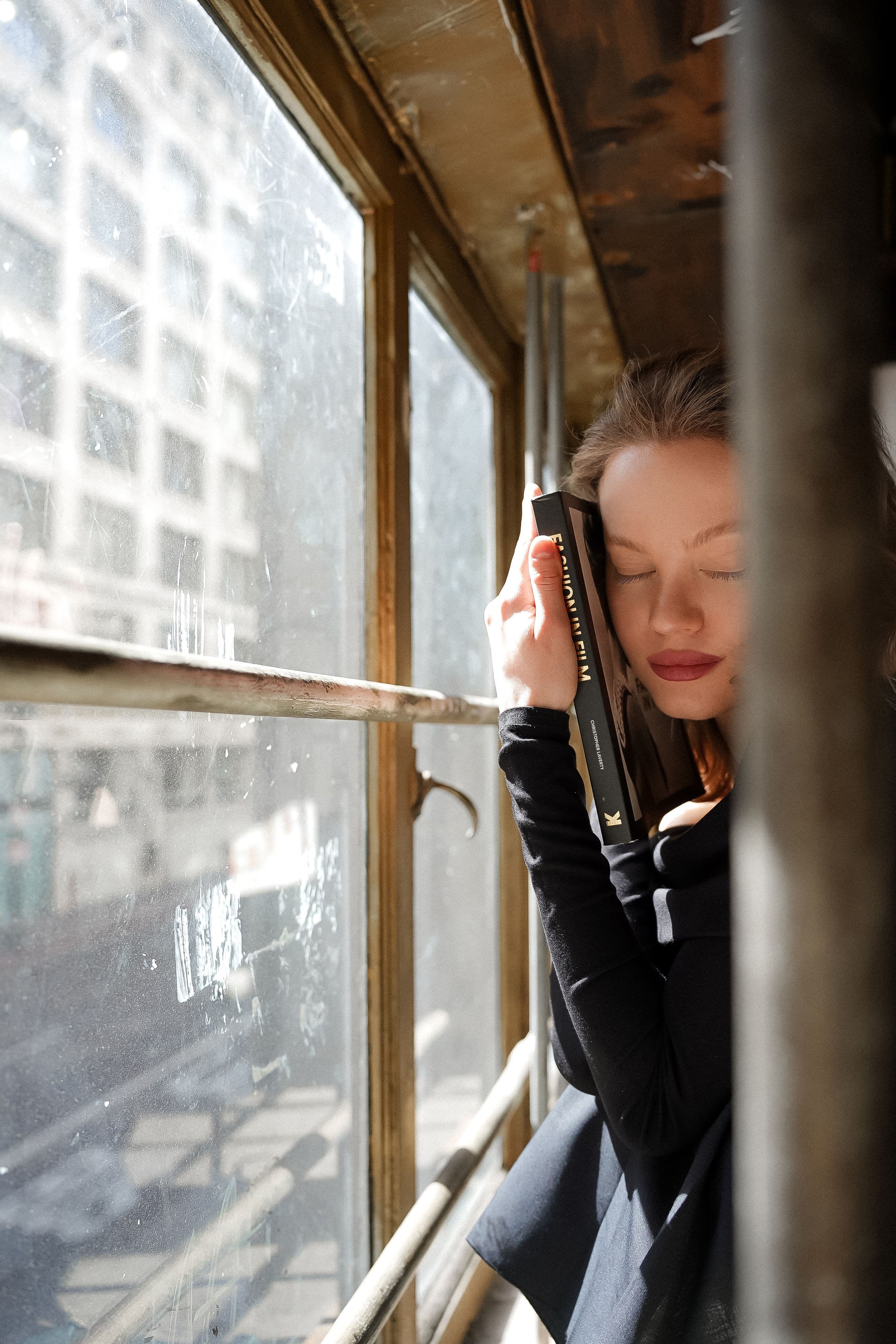 A reader holding a book close in the sunlight beside a city window